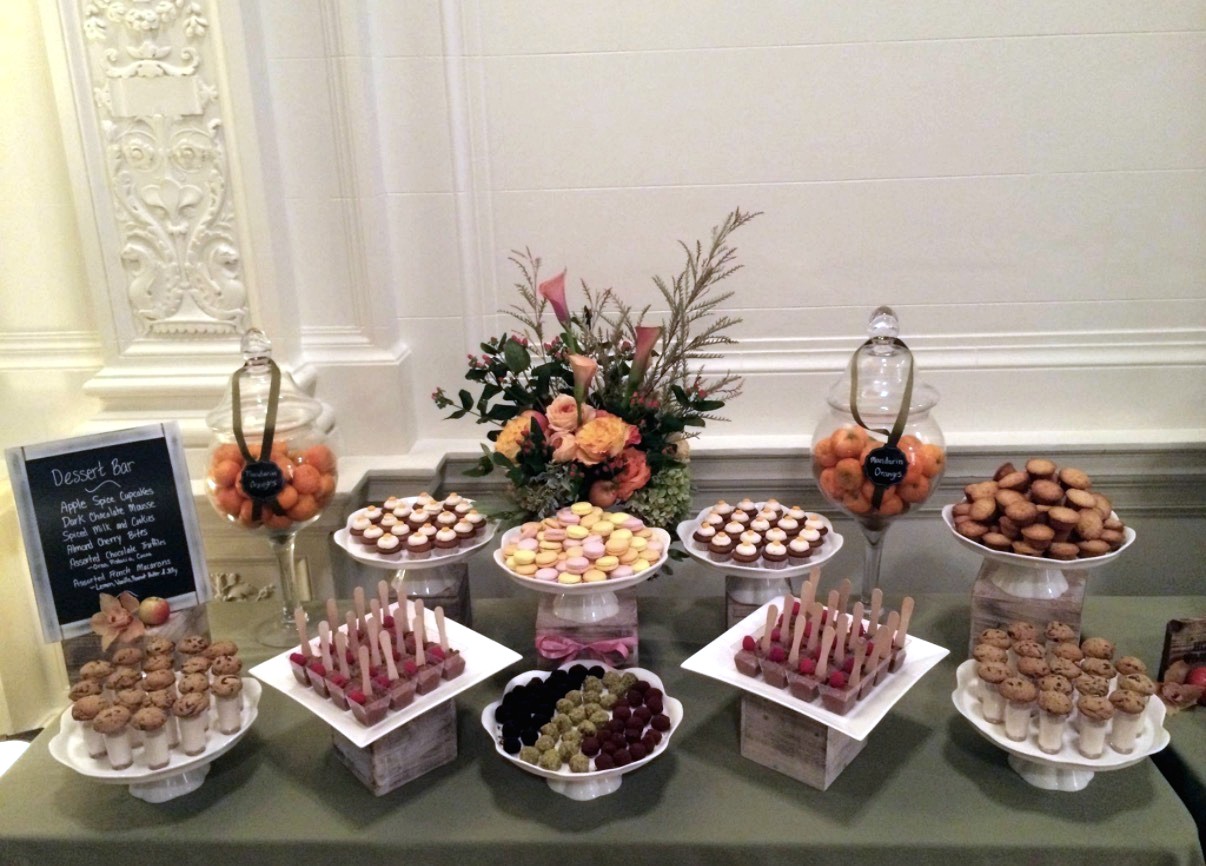 Formal dessert table with macarons, cupcakes, small bites, and flowers